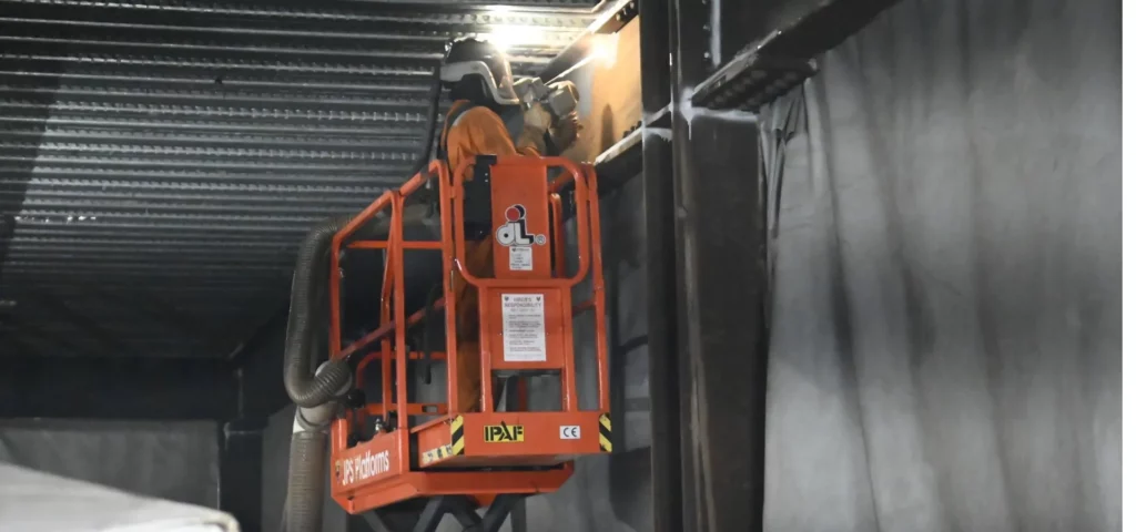 LaserTec technician working from a cherry picker to remove rust from structural steel beams with a handheld laser