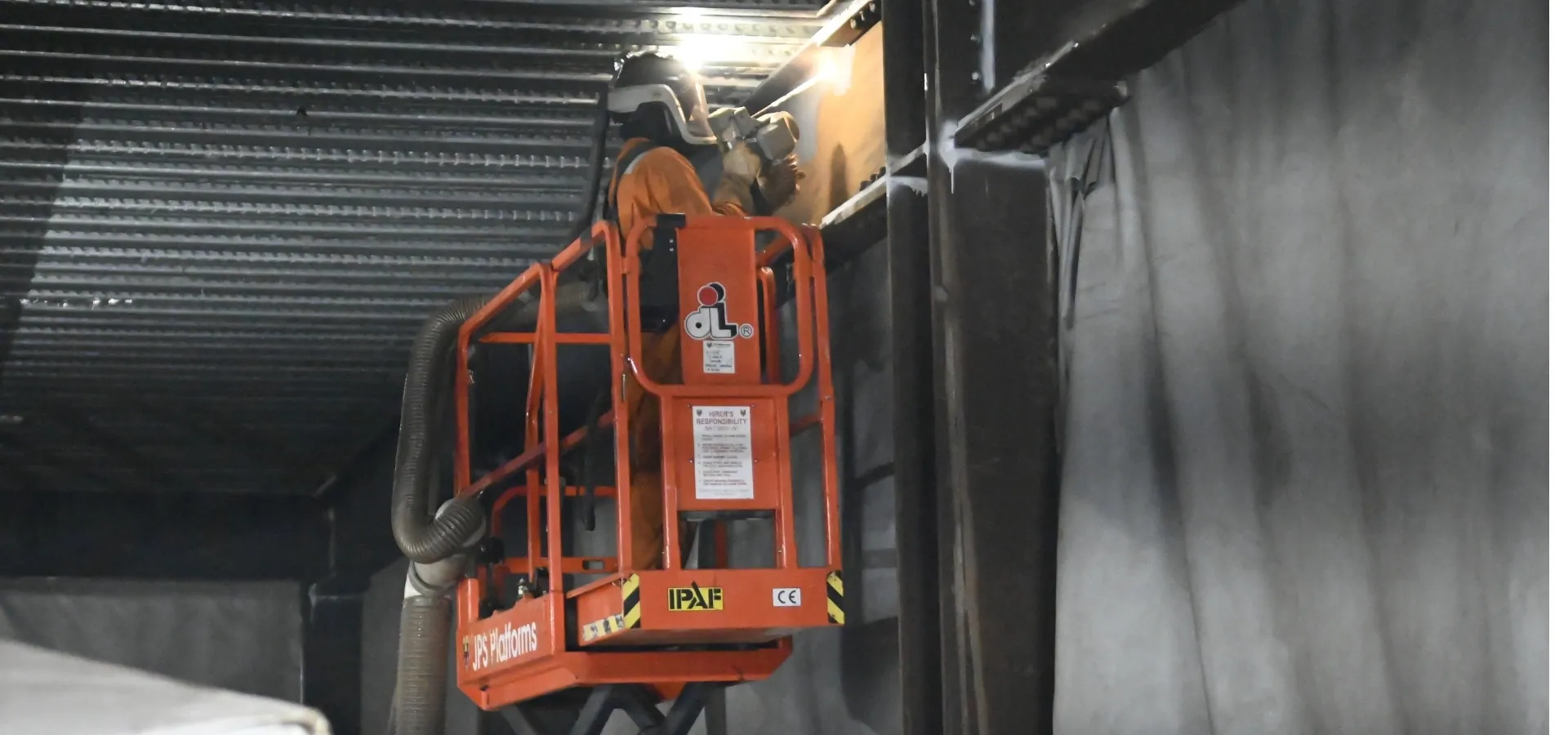 LaserTec technician working from a cherry picker to remove rust from structural steel beams with a handheld laser