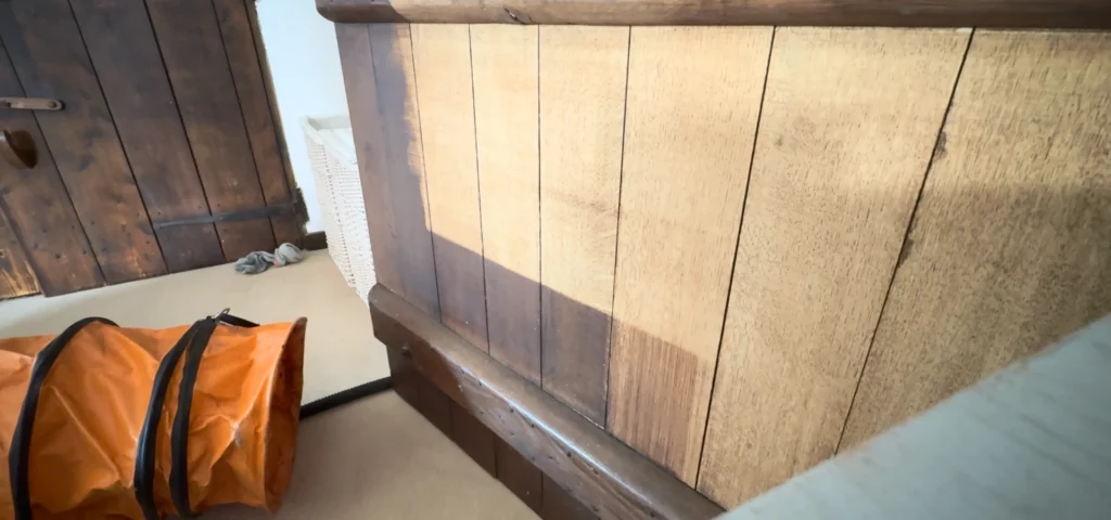 Oak panelling after laser varnish removal, showing bare timber with grain intact and a band of original dark varnish still remaining