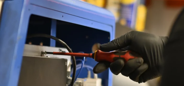 LaserTec engineer using an insulated screwdriver on a terminal block inside a laser cleaning machine