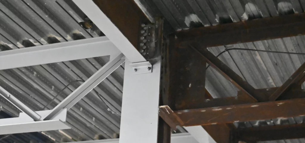 Structural steelwork part way through refurbishment, with rusted beams on one side and cleaned and recoated steel on the other
