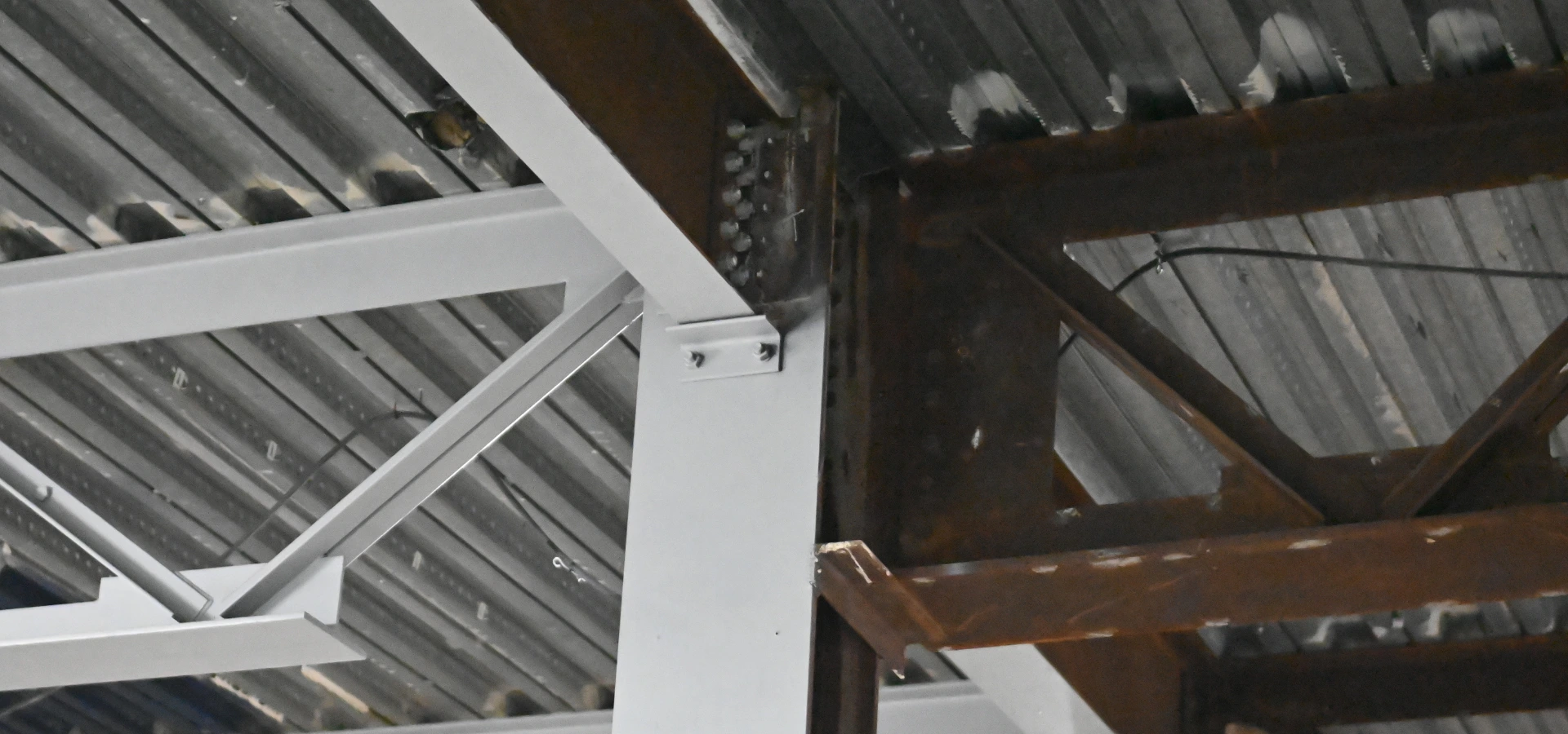 Structural steelwork part way through refurbishment, with rusted beams on one side and cleaned and recoated steel on the other